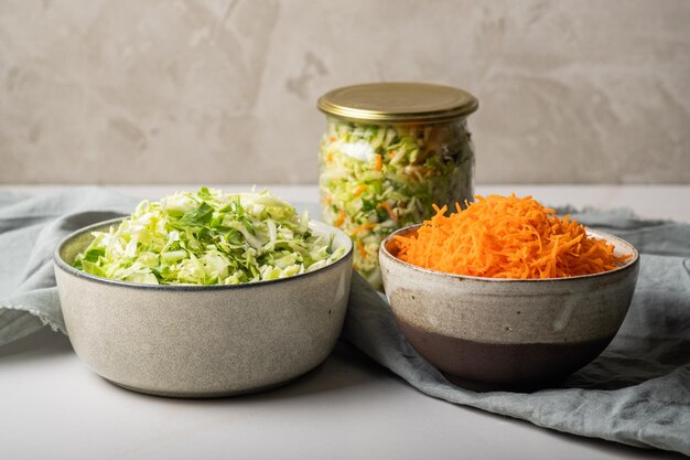 Hausgemachtes Sauerkraut in einem Glasgefäß auf einem grauen Tisch. Grünkohl und Karotten für Kohlsuppe schneiden.