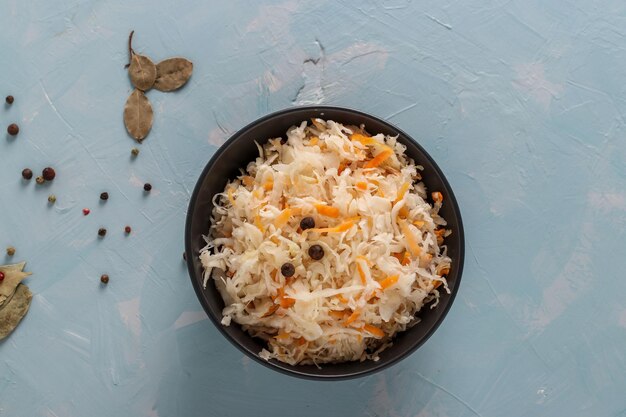 Hausgemachtes Sauerkraut mit Karotten in einer Schüssel auf hellblauem Hintergrund, Fermentiertes Essen, Ansicht von oben