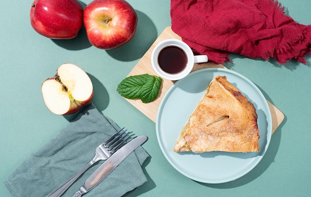 Hausgemachtes Stück Apfelkuchen mit frischen roten Äpfeln am grünen Tisch