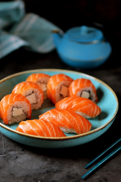 Hausgemachtes Sushi rollt Philadelphia und Nigiri in einem blauen Teller auf einer schwarzen Oberfläche.