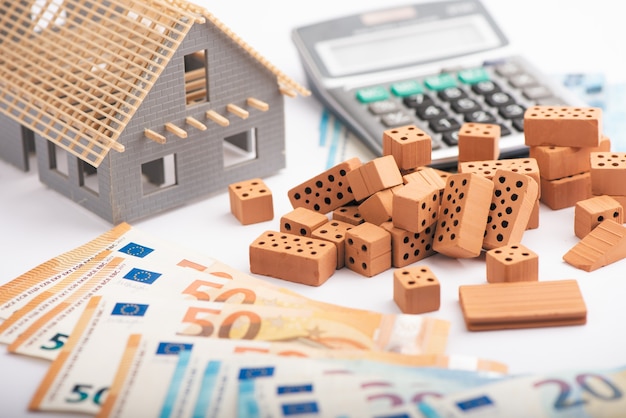Hauskauf Sparkonzept. Euro-Geldstapel mit rotem Haus und einem Taschenrechner