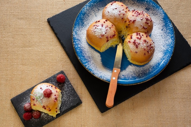 Hausmannskost-Konzept Frisches, hausgemachtes, süßes, weiches Milchbrot aus biologischem Anbau, gefüllt mit Sahne und dekoriert mit Himbeeren auf einem blauen Tellerkopierraum