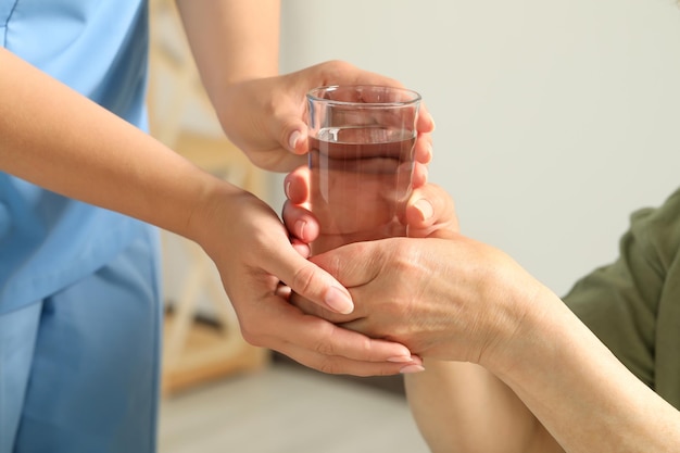 Hausmeister, der der älteren Frau drinnen ein Glas Wasser gibt, Nahaufnahme