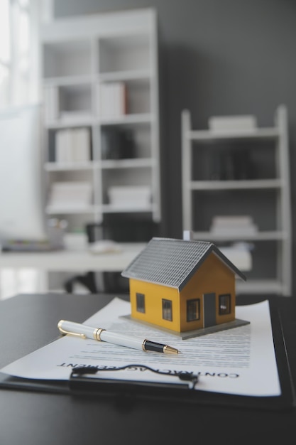 Hausmodell mit Immobilienmakler und Kunden, die über einen Vertrag zum Kauf einer Hausversicherung oder eines Darlehens im Immobilienhintergrund diskutieren