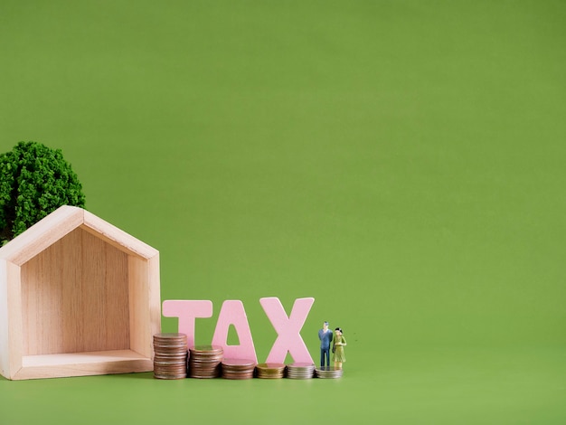 Hausmodell mit Wortsteuer, Miniaturmenschen und Münzen auf grünem Hintergrund. Platz für Text