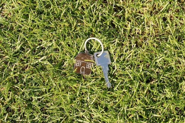 Foto hausschlüssel mit einem schlüsselanhänger in form eines hauses auf grünem gras