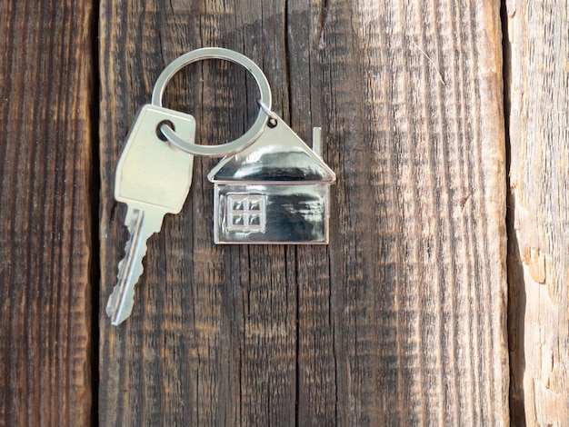 Hausschlüssel und Schlüsselanhänger in Form eines Hauses auf Holzgrund mit einem Platz für Textkonzepte für Immobilienumzug oder Vermietung von Immobilien