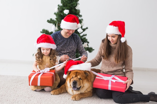 Haustier, Feiertage und festliches Konzept - Familie mit Hund sitzt auf dem Boden in der Nähe des Weihnachtsbaums.