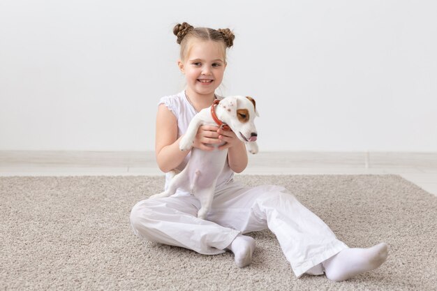 Haustier-, Kinder- und Tierkonzept - Lächelndes Kindermädchen, das mit Welpen Jack Russell Terrier sitzt.