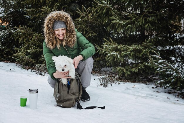 Haustierpflege in der Winterkaltjahreszeit glückliche Frau und maltesischer Hund im Rucksack, der Spaß hat und