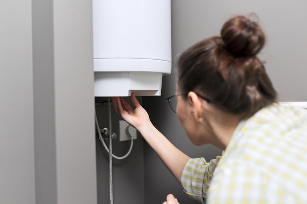 Hauswarmwasserbereiter, eine Frau regelt die Temperatur an einem elektrischen Warmwasserbereiter, Komfort und Warmwasser im Haus