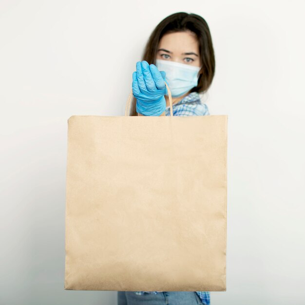 Hauszustellung bei Coronavirus, Virusausbrüchen und Pandemien. Mädchen in blauen Handschuhen hält eine Tasche mit Produkten auf einem weißen isolierten Hintergrund. COVID-19
