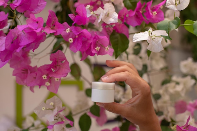 Hautcrememodell, weiße Flasche in weiblichen Händen auf rosa Blumenhintergrund, Hautsicherheit