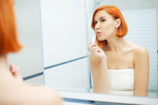 Hautpflege. Frau mit roten Haaren macht Make-up im hellen Badezimmer.