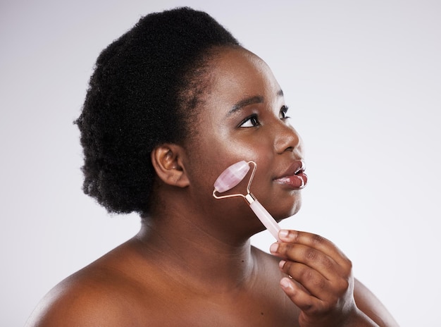 Hautpflege Gesicht und Massage mit einer vorbildlichen schwarzen Frau im Studio auf grauem Hintergrund mit einer Walze Gesichtsluxus und Schönheit mit einer jungen Frau in Übergröße im Innenbereich, um ein Anti-Aging-Produkt zu fördern