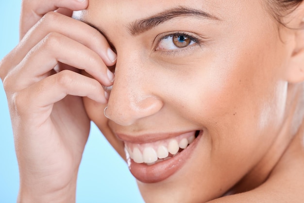Hautpflege-Make-up und Lächeln einer Frau für Schönheitskosmetik und Dermatologie vor blauem Hintergrund im Studio Spa-Gesichtsaugen und Porträt eines Kosmetikmodells, das mit Gesichtskosmetik zufrieden ist