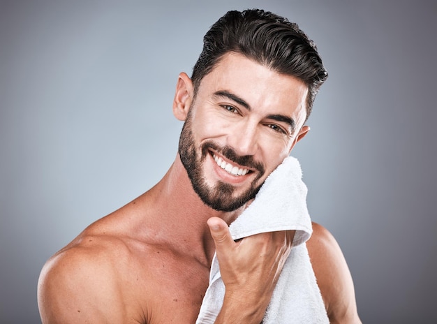Hautpflege-Wellness und Porträt eines glücklichen Mannes in einem Studio mit einer natürlichen Selbstpflege- und Gesichtsroutine Gesundheitsdermatologie und männliches Modell mit einem Gesichtstuch zur Behandlung isoliert durch grauen Hintergrund
