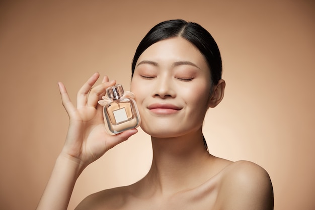 Hautpflegekonzept - charmante junge asiatische Frau, die Flaschenspray und Lotion mit perfekter Make-up-Fotokomposition des brünetten Mädchens hält