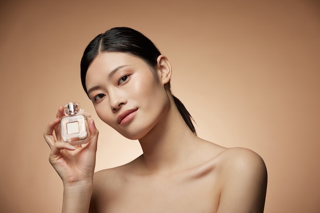 Hautpflegekonzept - charmante junge asiatische Frau, die Flaschenspray und Lotion mit perfekter Make-up-Fotokomposition des brünetten Mädchens hält