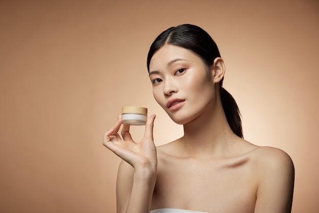 Hautpflegekonzept - charmante junge asiatische Frau, die Flaschenspray und Lotion mit perfekter Make-up-Fotokomposition des brünetten Mädchens hält