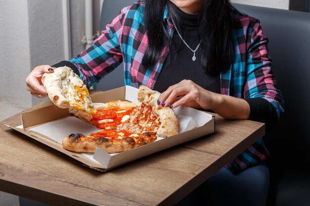 Hay una caja con diferentes tipos de pizzas y shawarma sobre la mesa, las manos de las mujeres sostienen,