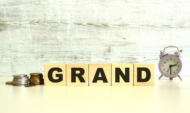 Hay cinco cubos de madera con letras en la mesa al lado de las monedas GRAN palabra Sobre un fondo gris Conceptos de vista frontal