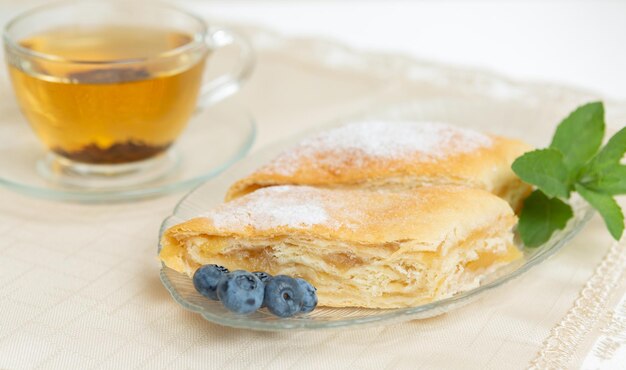 Hay dos rebanadas de tarta de manzana, arándanos y hojas de menta en el plato, una taza de té al lado.