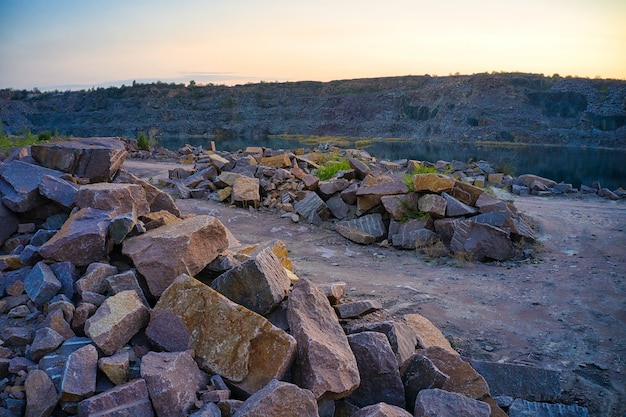 Hay grandes montones de cantos rodados a la cálida luz del atardecer en el territorio de una antigua cantera de piedra inundada.