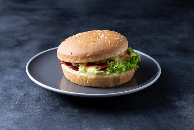 Hay una hamburguesa en la mesa en un plato. Sobre un fondo negro.