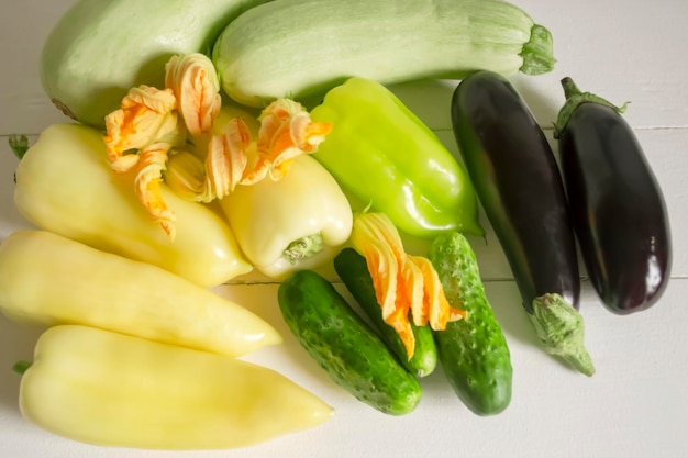 Hay un montón de verduras de verano en la mesa blanca pimientos calabacín y flores de calabacín verduras de berenjena para vegetarianos