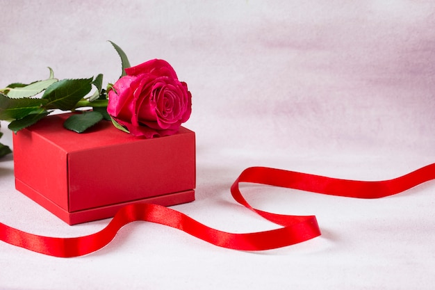 Hay una rosa roja en la caja de regalo roja y una cinta roja al lado.