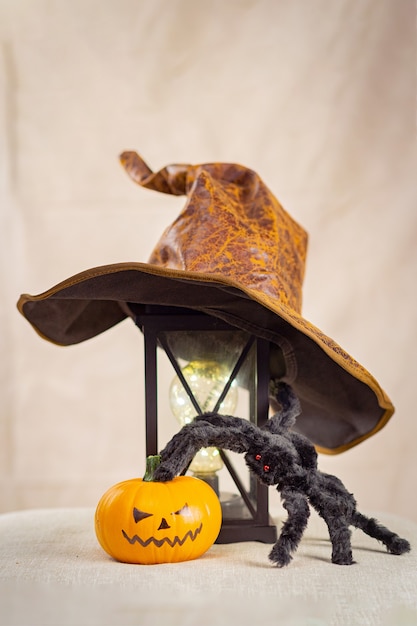 Foto hay un sombrero de bruja en una lámpara antigua, una araña peluda negra con ojos rojos y una calabaza de halloween al lado.