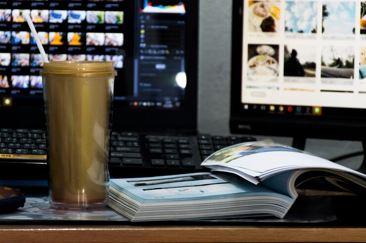 Foto hay una taza dorada sobre la mesa y un libro junto a ella. y con el fondo, es una computadora portátil y un monitor de computadora.