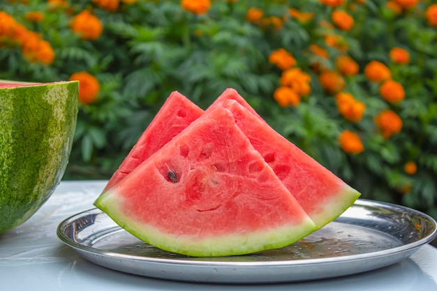 Hay varias piezas de sandía en la bandeja flores de naranja de verano están en el fondo