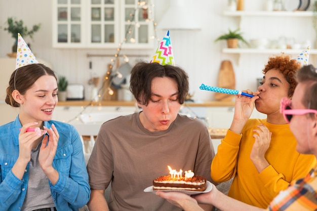 Haz un deseo hombre con gorra de fiesta soplando velas encendidas en la torta de cumpleaños feliz fiesta de cumpleaños