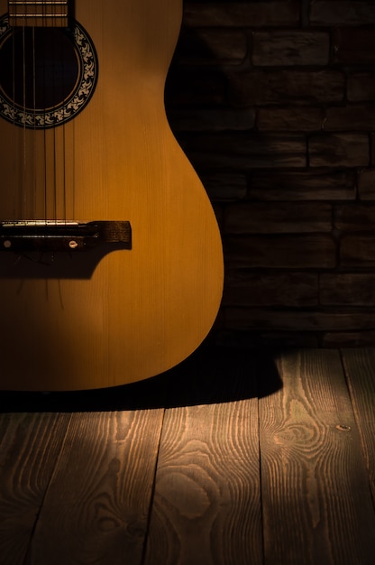 Un haz de luz ilumina una guitarra acústica de pie contra una pared en un piso de madera.