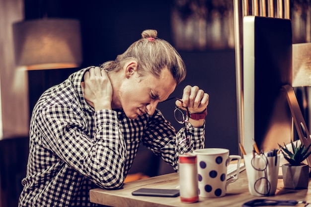 Haz una pausa. Hombre preocupado apoyando los codos sobre la mesa y manteniendo los ojos cerrados