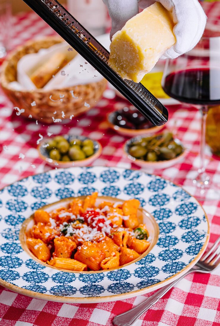 He grates queso al plato con pasta de penne fresca