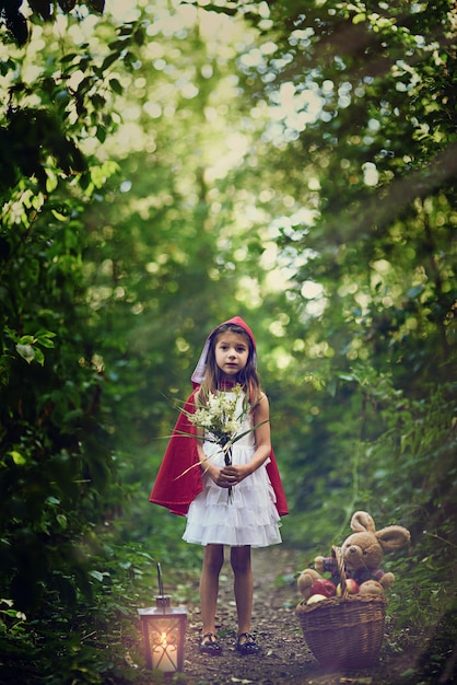 He recogido estas bonitas flores a lo largo del camino Fotografía de una niña pequeña vestida con una capa roja sosteniendo algunas flores en el bosque