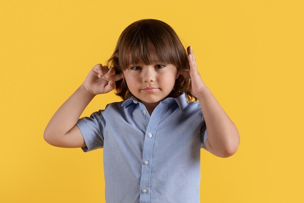 Hear no evil Niño obstinado cerrando los oídos con las manos no quiere escuchar mirando a la cámara con fondo naranja