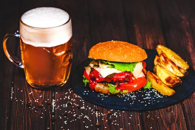 Hecho en casa, deliciosa hamburguesa de ternera con lechuga y patata, un vaso de cerveza servido sobre una tabla para cortar piedra. Oscuro