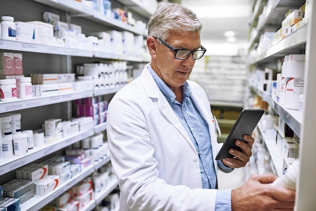 De hecho, podría tomar algo de esto más tarde. Fotografía de un farmacéutico maduro y concentrado que toma notas de las existencias de medicamentos en los estantes de una farmacia.