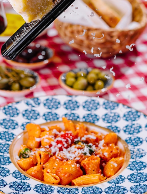 Foto hef reibt käse auf den teller mit frischer penne-pasta