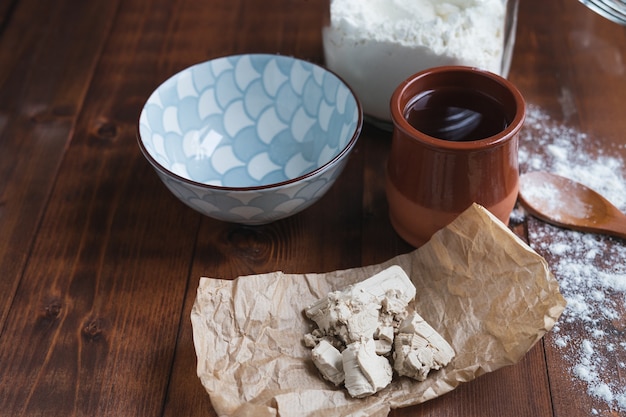 Hefestücke auf Papier mit Behältern und Zutaten auf Holzbasis zur Herstellung von Sauerteig. Bäckereikonzept.