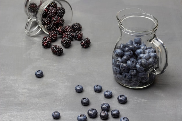 Heidelbeeren in einer Karaffe mit Wasser Brombeeren werden aus einem Glas verstreut