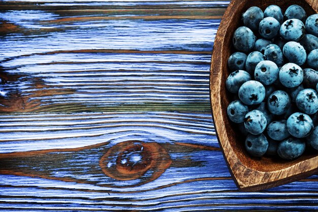 Heidelbeeren in herzförmiger Holzschale auf Holzbrett