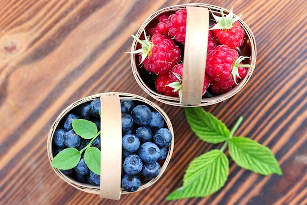 Heidelbeeren und Himbeeren in kleinen Körben aus Birkenrinde auf Holzhintergrund Ernte von wi