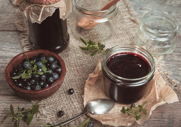 Heidelbeermarmelade im Glas mit Beeren und Blättern über rustikalem Holztisch