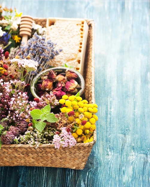 Heilende Kräuter und Blumen für Kräutertee in einem Behälter und in einer Wabe auf einer Draufsicht des blauen hölzernen Hintergrundes liegen flach