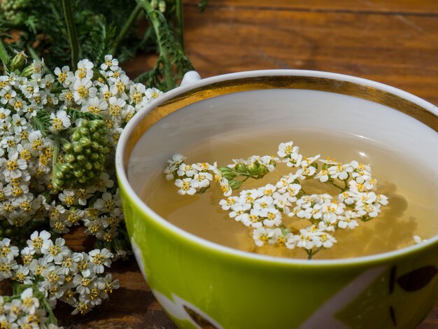 Foto heilpflanze schafgarbe, ein becher mit einer abkochung von schafgarbenblüten auf holzhintergrund